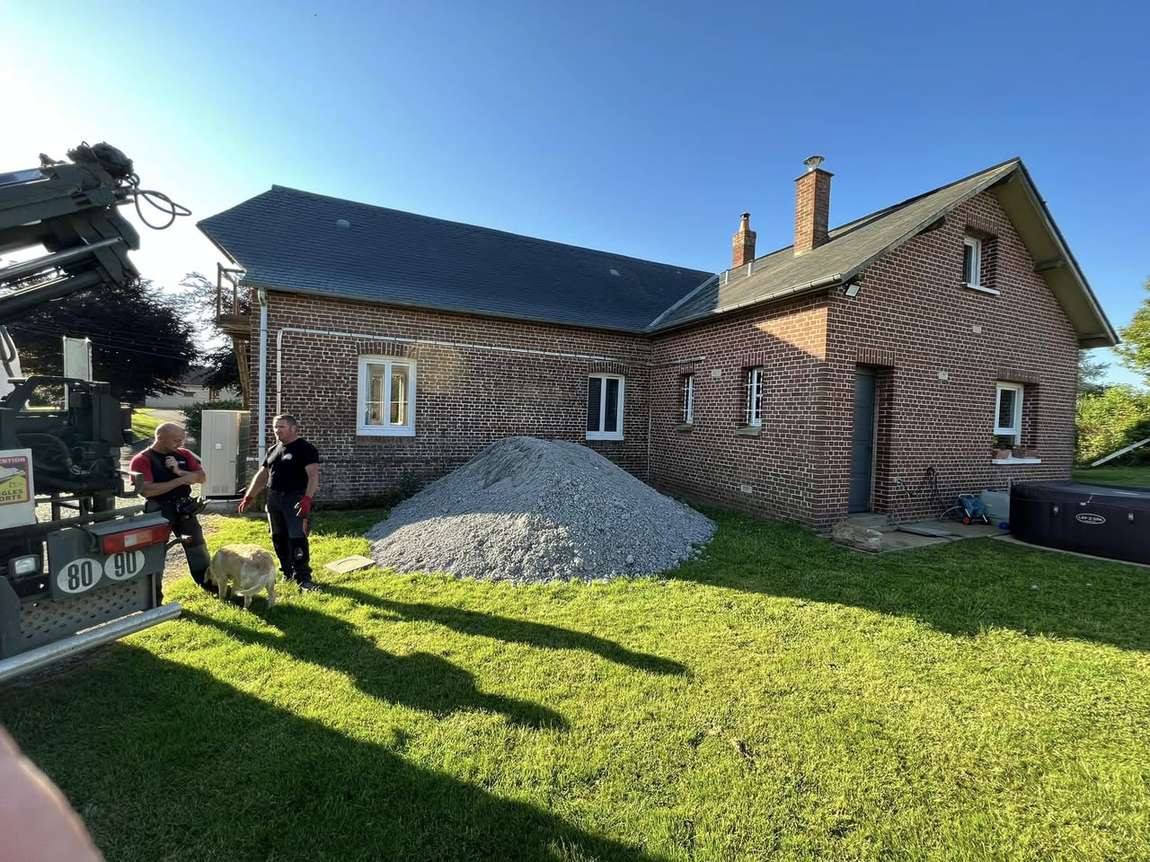 Camion-grue livrant du gravier devant une maison en brique, avant la construction de l'extension