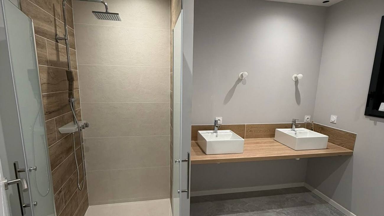 Salle de bain complète avec douche carrelée et double vasque sur plan aspect bois, réalisée par BAT & CO Construction