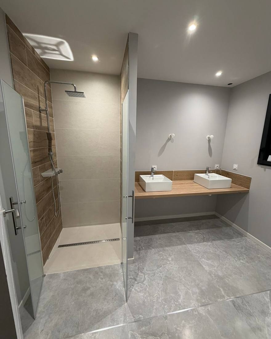 Salle de bain refaite avec douche à l'italienne carrelée et double vasque sur plan en bois