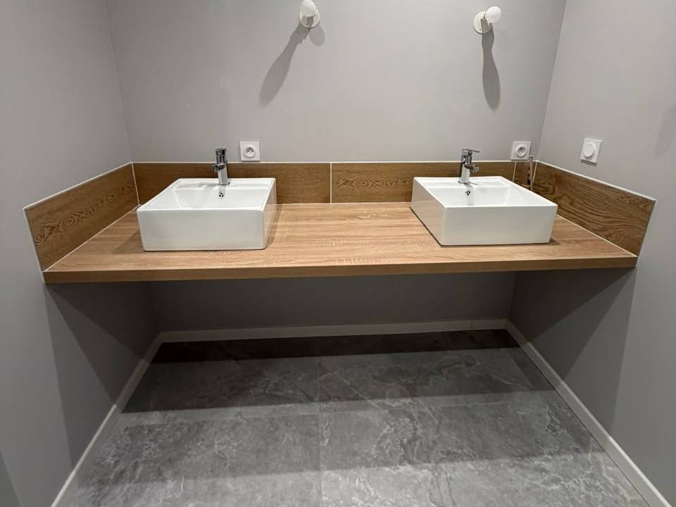 Double vasque blanche posée sur un plan aspect bois, murs gris et grand carrelage gris au sol