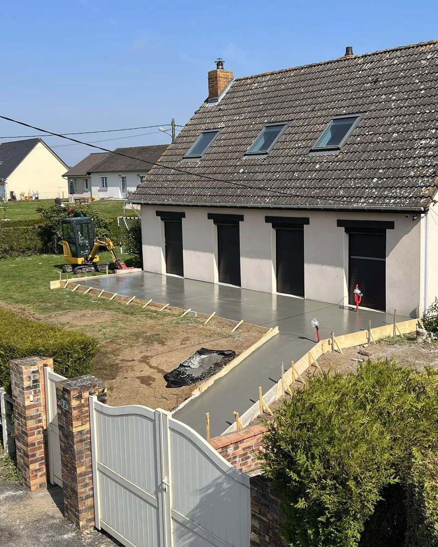 Dalle béton coulée avec sa rampe d'accès entre le portail et la façade d'une maison, mini-pelle sur le côté